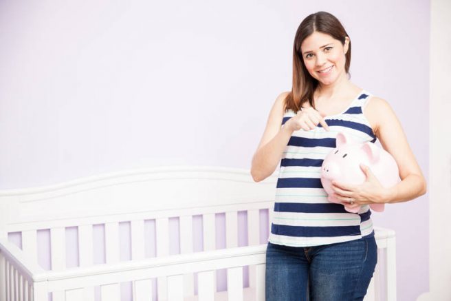 Femeie gravida care tine in mana o pusculita in forma de porc, economisind pentru bebelus