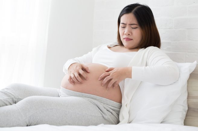 femeie-gravida-asiatica-care-are-colestaza-se-scarpina-pe-burtica-si-tine-ochii-inchisi