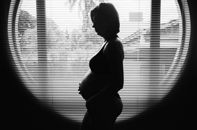 Femeie însărcinată stând în fața ferestrei