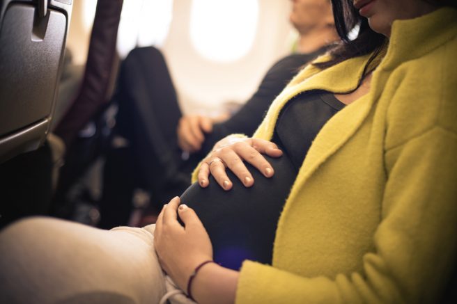 Femeie însărcinată care călătorește cu avionul și se ține de burtică