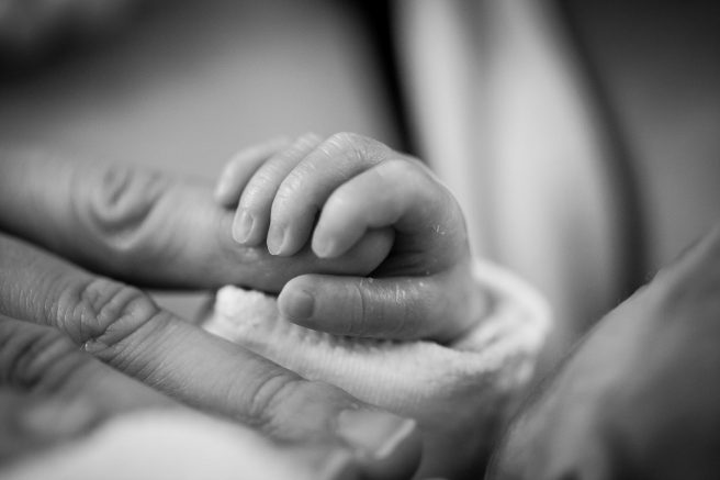 Mână de bebeluș care ține degetul mamei