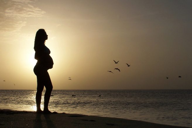 Femeie însărcinată pe plajă la răsărit