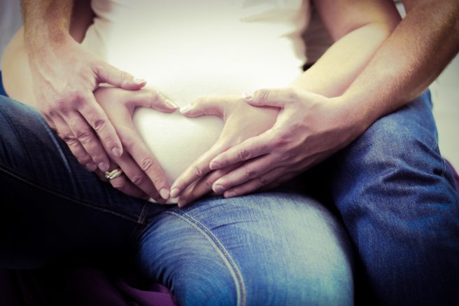 Femeie însărcinată și mâinile soțului pe burta acesteia