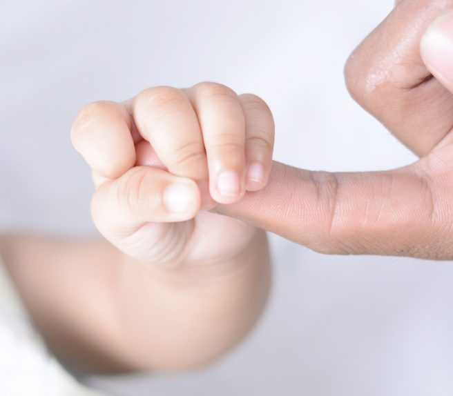 Mâna unui bebeluș care ține un deget de adult