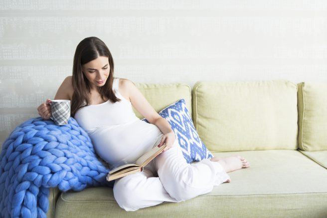 Femeie însărcinată care citește și bea
ceai cald 