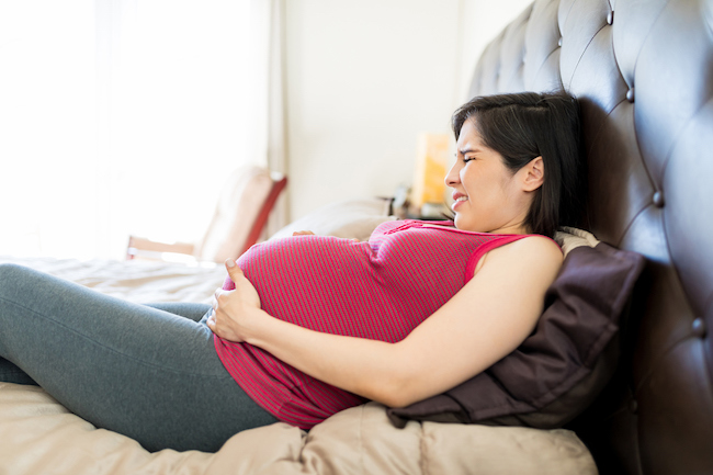 femeie-brunetă-gravidă-cu-maiou-roșu-care-se-ține-de-burtă-și-are-contracții-puternice