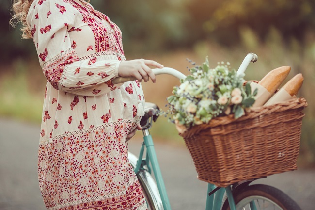 femeie-gravida-cu-rochie-cu-flori-are-o-bicicleta-langa-ea-cu-un-cos-cu-flori-pentru-lucruri-grele-in-sarcina