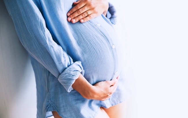 femeie-gravidă-în-cămașă-albastru-deschis-care-stă-cu-mâinile-pe-burtă