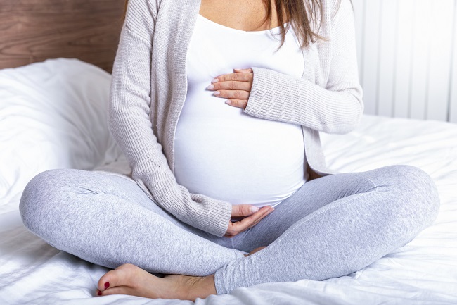femeie-gravidă-cu-triplu-test-care-stă-ghemuită-în-pat-și-cu-mâinile-pe-burtă