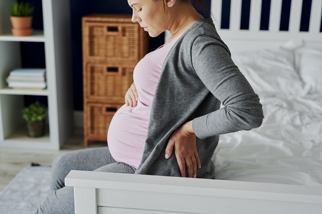femeie-gravidă-cu-tricou-roz-care-stă-pe-pat-și-are-dureri-de-spate-ca-simptom-pentru-anemia-în-sarcină