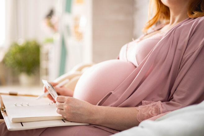 femeie-însărcinată-care-stă-întinsă-în-patși-are-o-agentă-în-brațe-și-scrie-o-scrisoare-de-dragoste